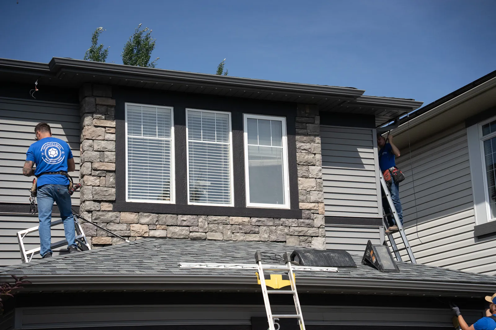 Two Gemstone Lights installers fitting track lighting along the roofline of a home
