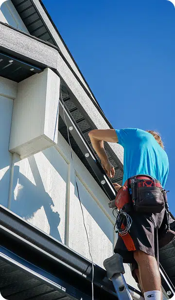 An installer fastening track under a roofline from a ladder