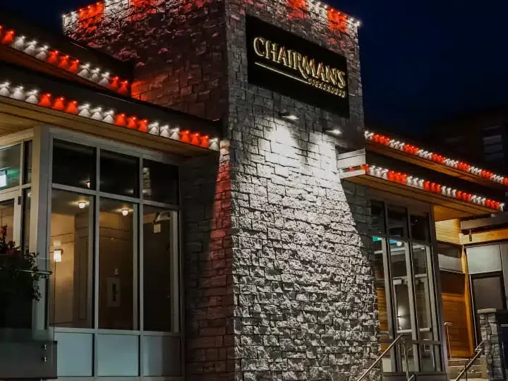 Stone-clad restaurant entrance at night with red and white lights along each roofline