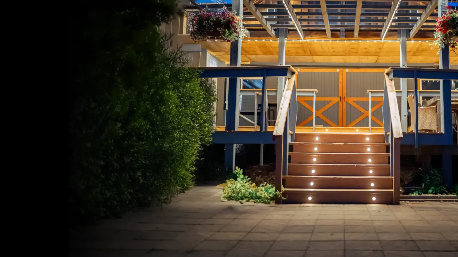 Deck stairs under a lit pergola at night, with small warm lights in every tread