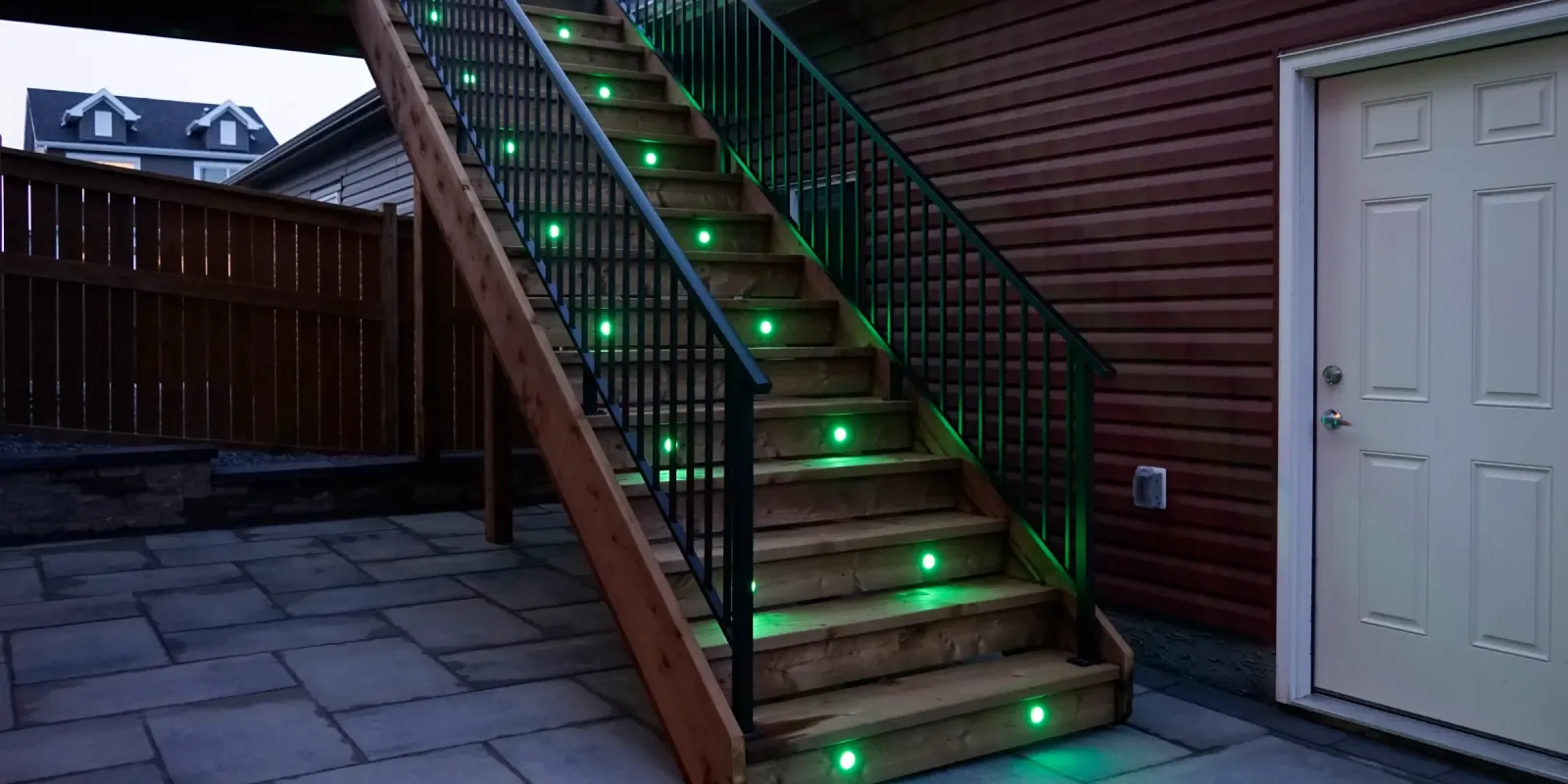 Outdoor stairs beside a house with a green smart light glowing in every tread