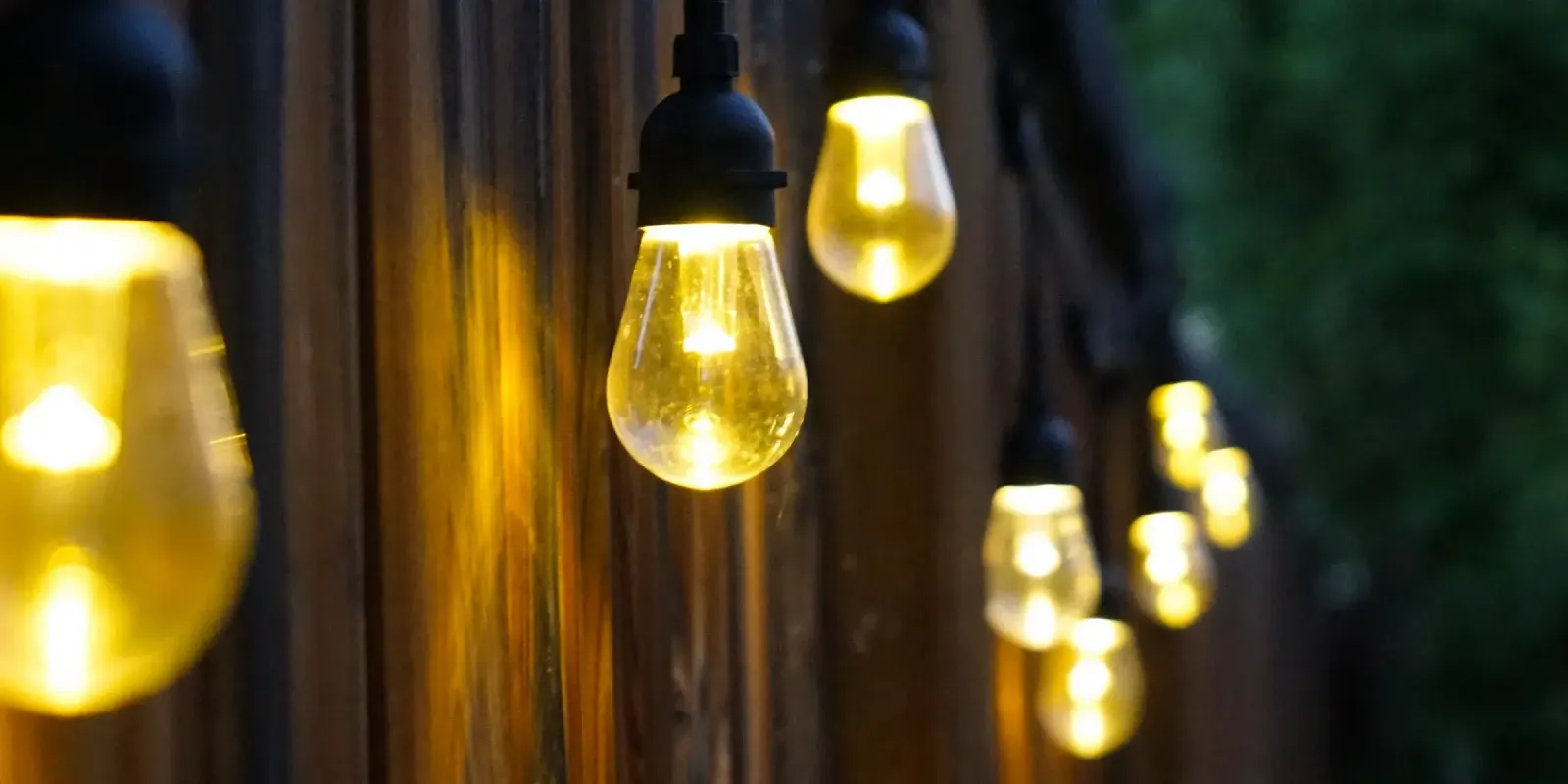 Close view of warm white smart patio bulbs glowing against a dark wooden fence