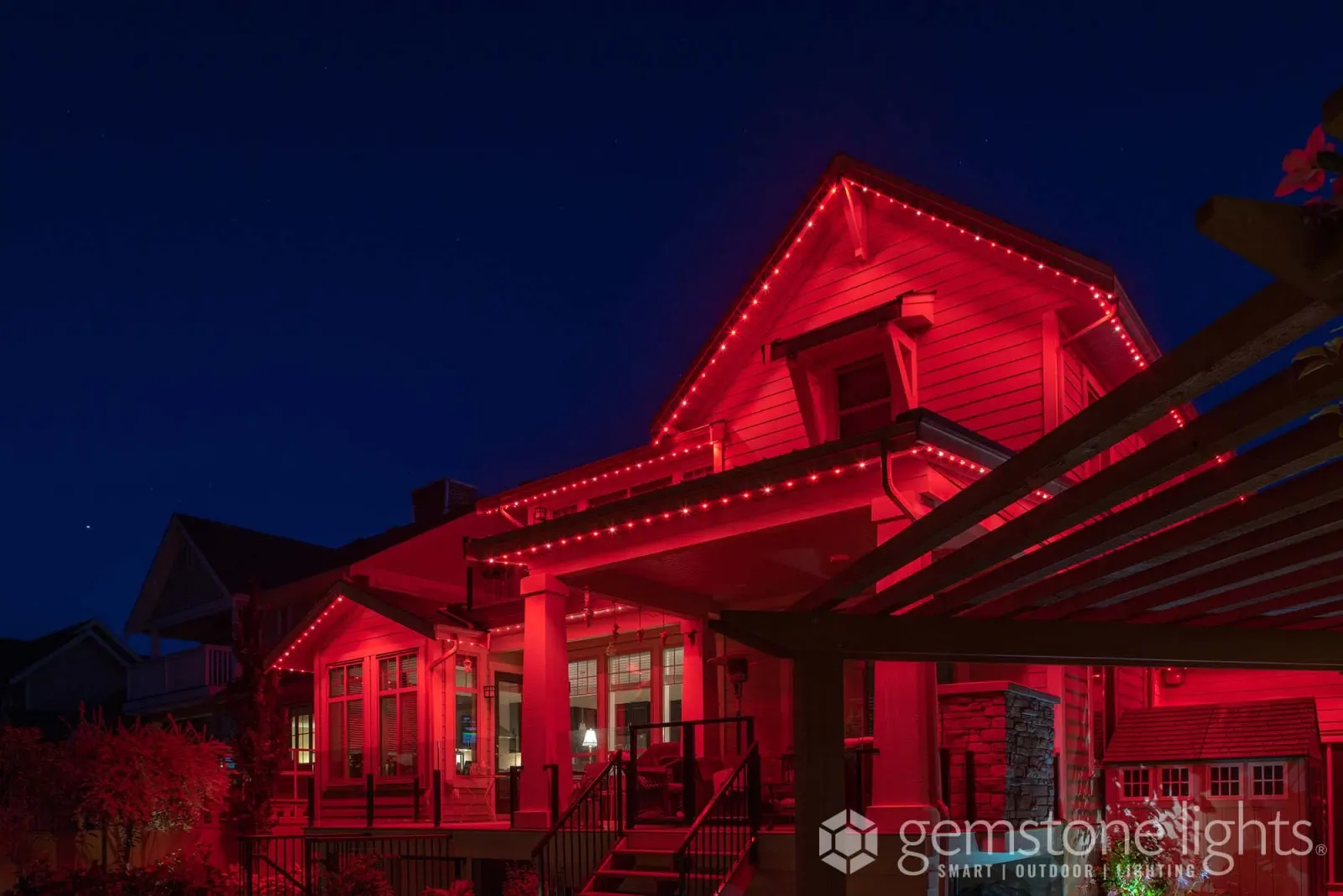 Front porch and pergola of a home lit in deep red, with lights along the roofline above