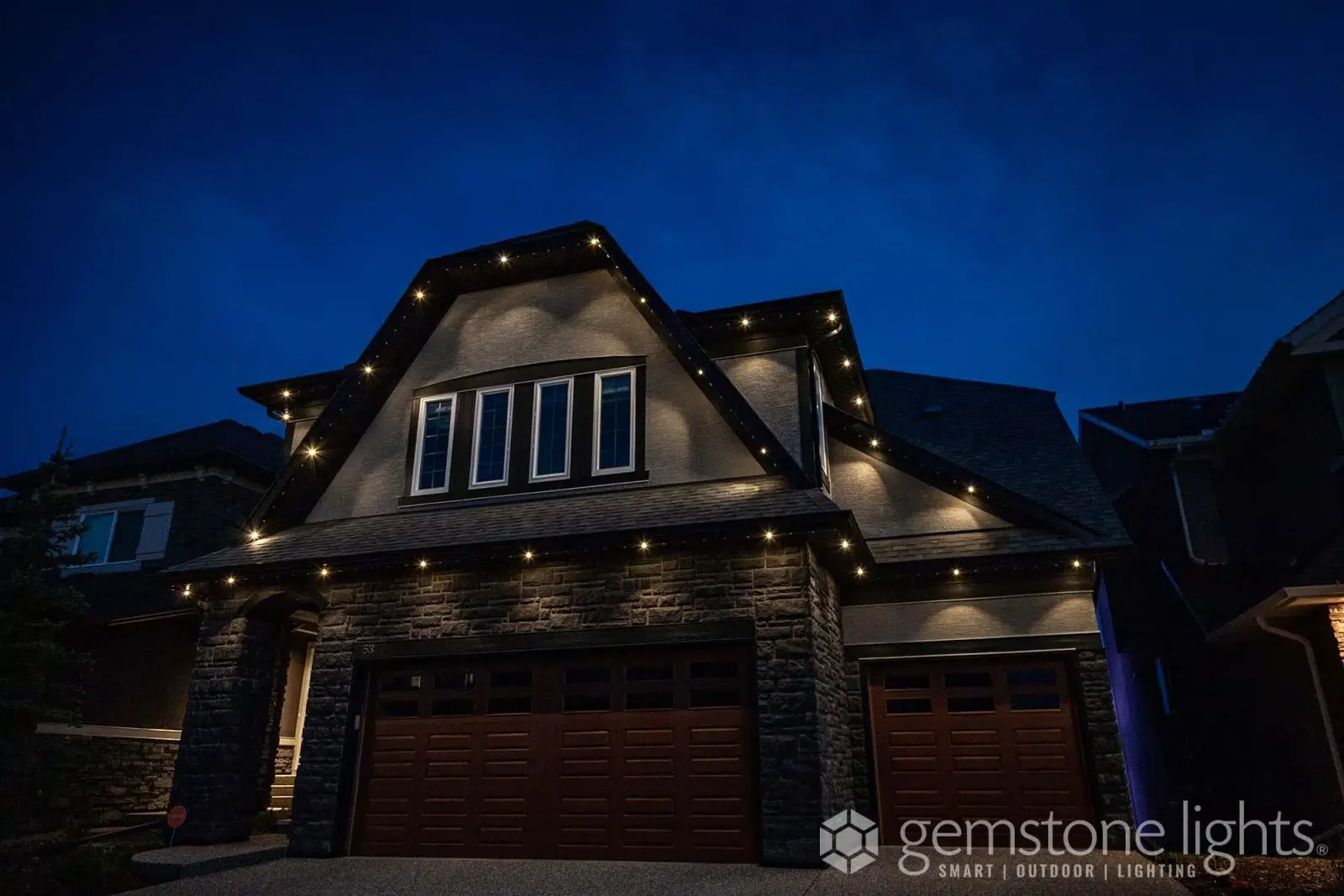 Two-story home with multiple gables outlined in crisp warm white lights at dusk