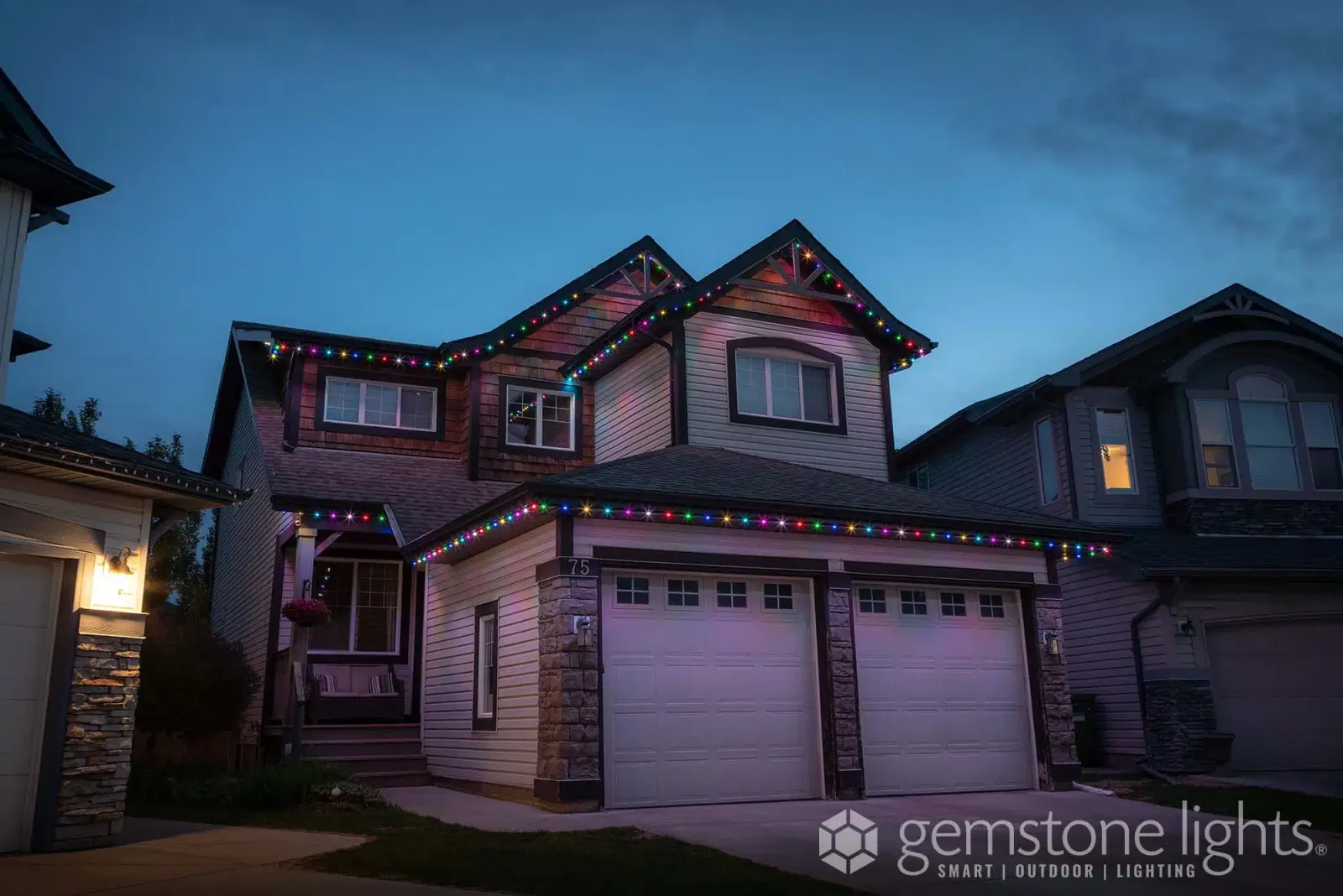 Two-story brick home with a covered porch and warm white lights along the roofline