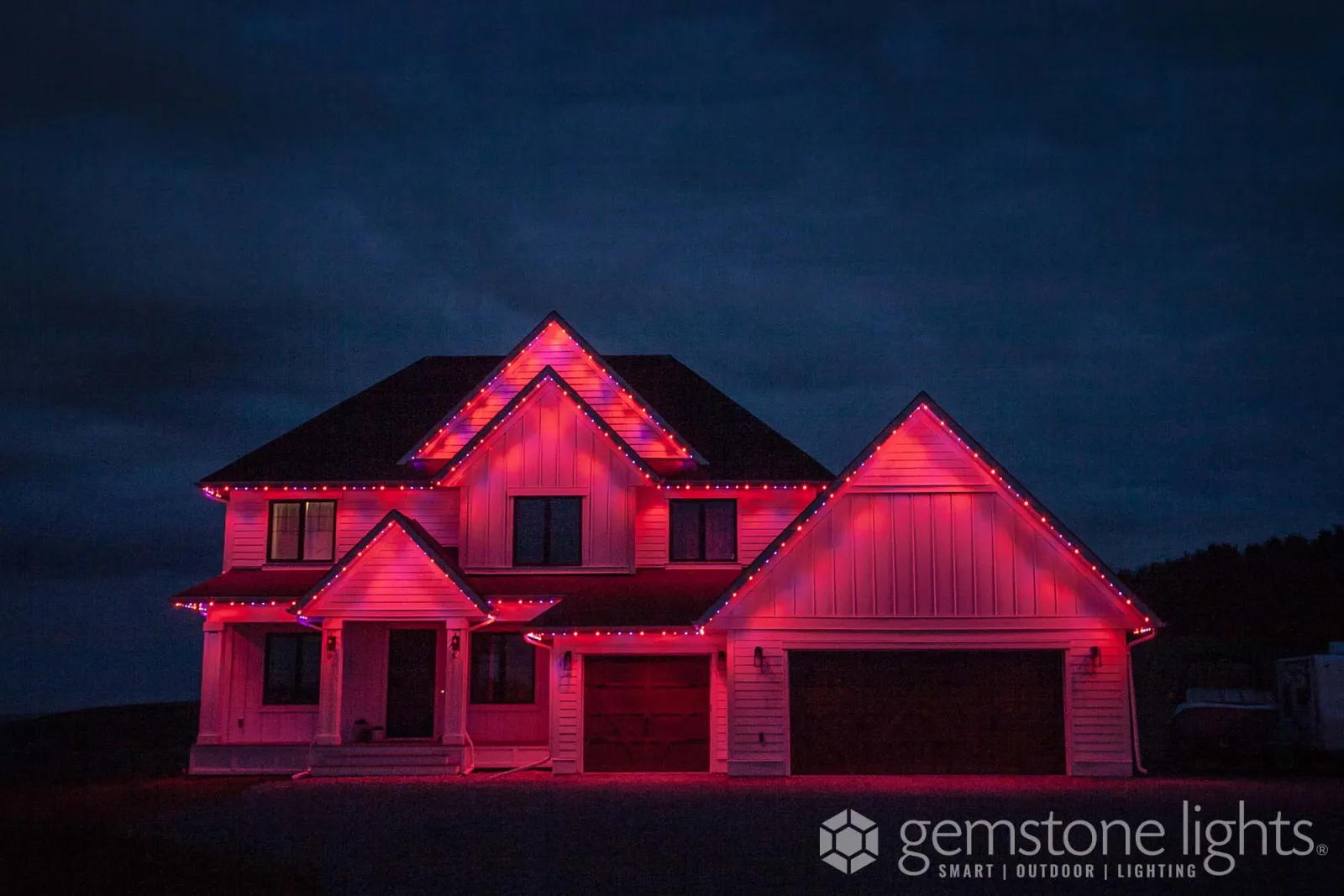 Farmhouse-style home with white siding and twin gables washed in red light at twilight