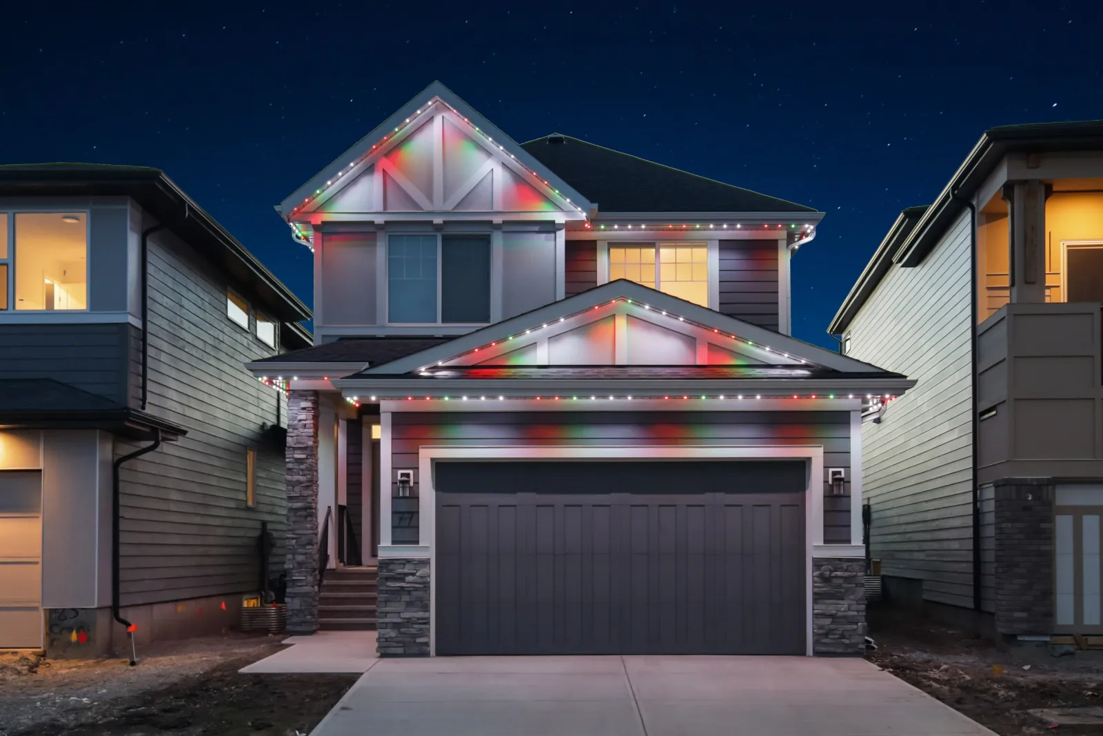 The same house at dusk with red, green and white Christmas lights along every roofline