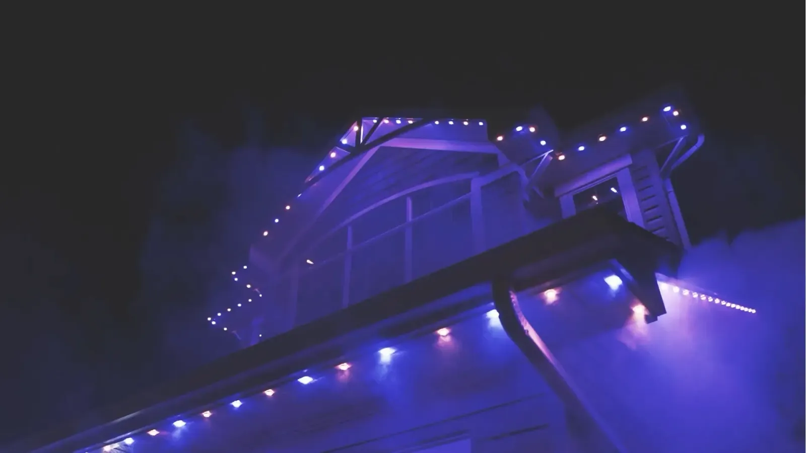 Roofline and gutter edge lit purple and blue against a dark night sky
