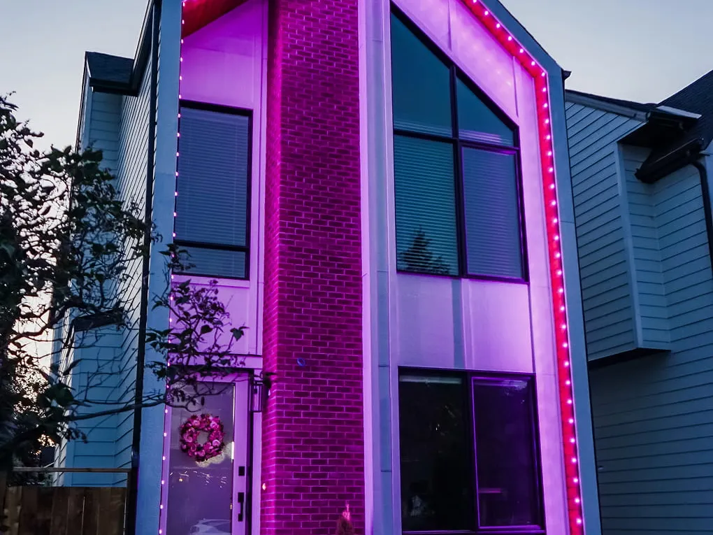 Narrow modern home with tall windows, its outline and brick wall glowing pink and purple